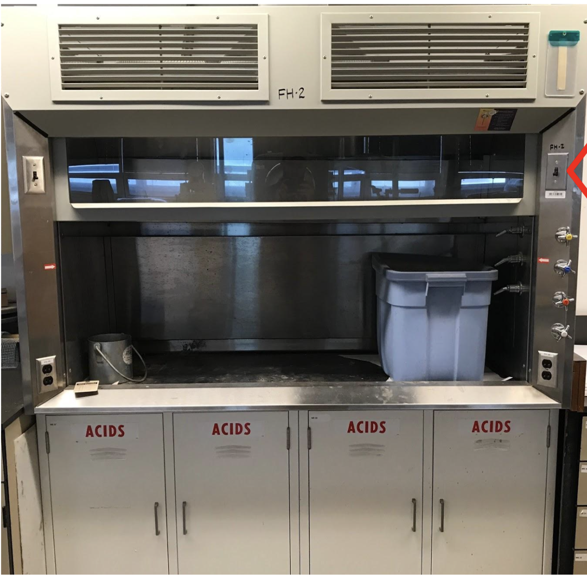 pictured is an unused fume hood storing a blue tub above cabinets labeled "acid".